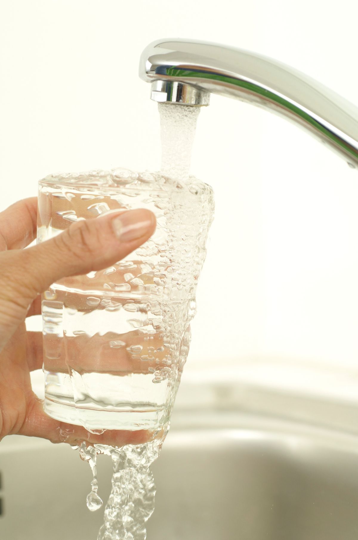 Close-up of a hand holding a glass as tap water fills it