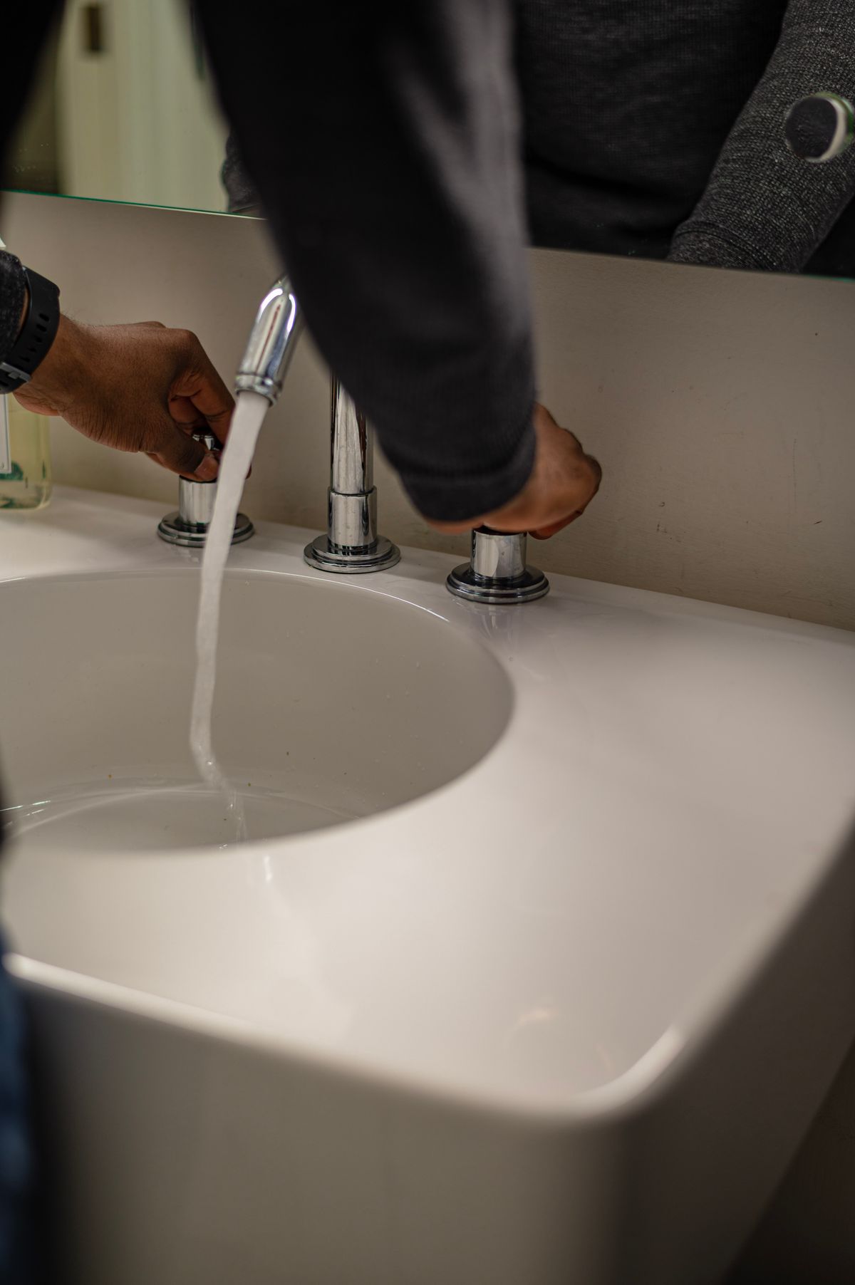 Close-up of hands adjusting water flow in a modern ceramic sink
